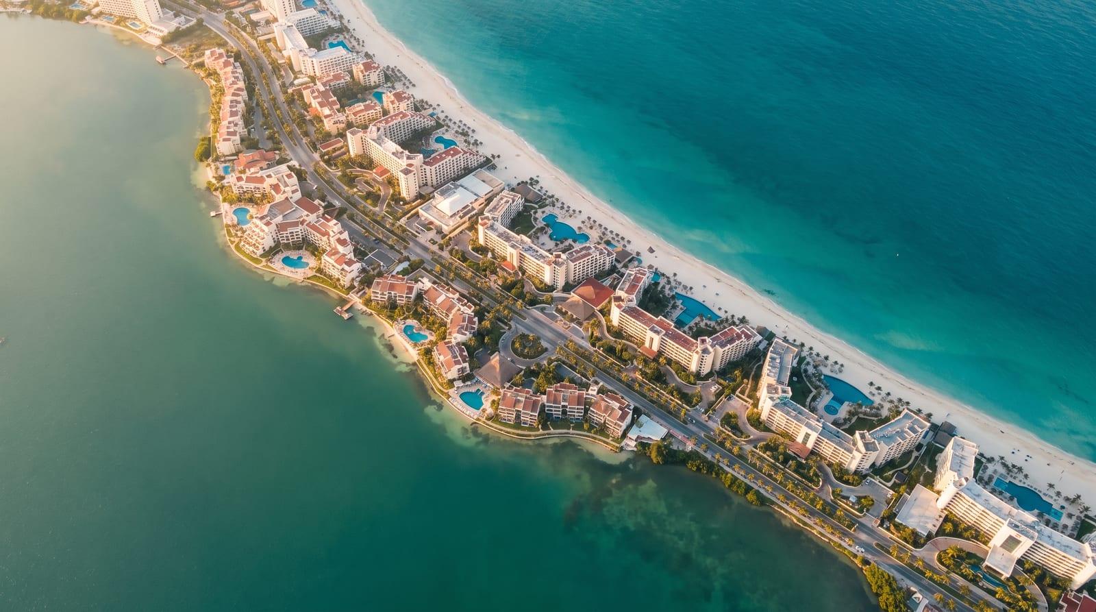 Letecký pohled na zahnutou hotelovou zónu Cancúnu mezi tyrkysovým Karibikem a lagunou Nichupté.