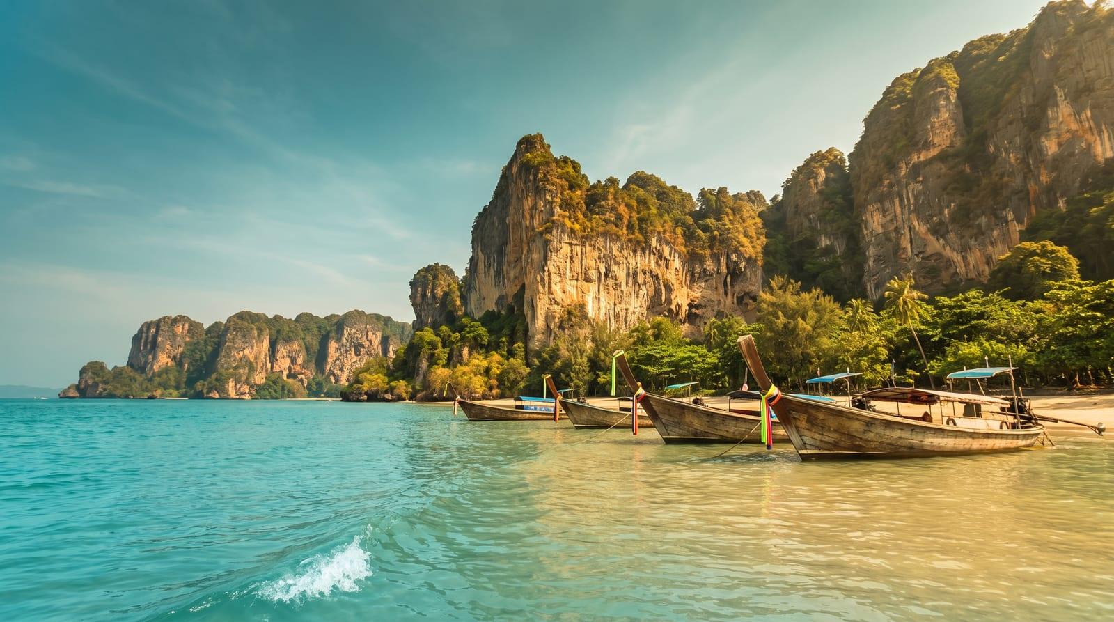 Vápencové útesy nad tyrkysovou zátokou Railay v Krabi s dlouhými čluny u pláže