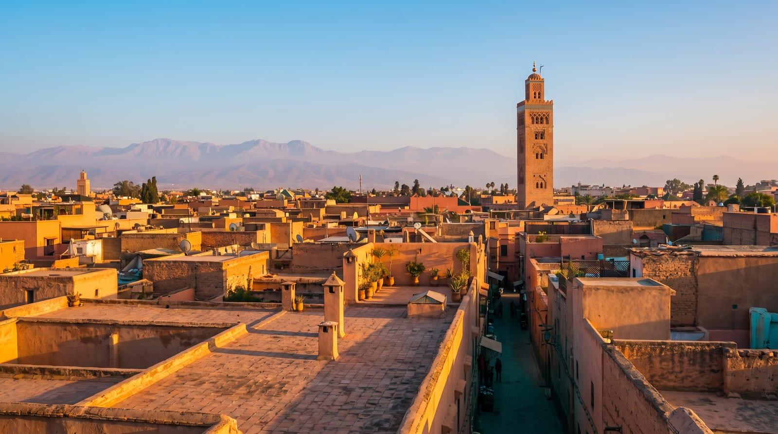 Střechy mediny v Marrákeši s minaretem mešity Koutoubia a pohořím Atlas v pozadí